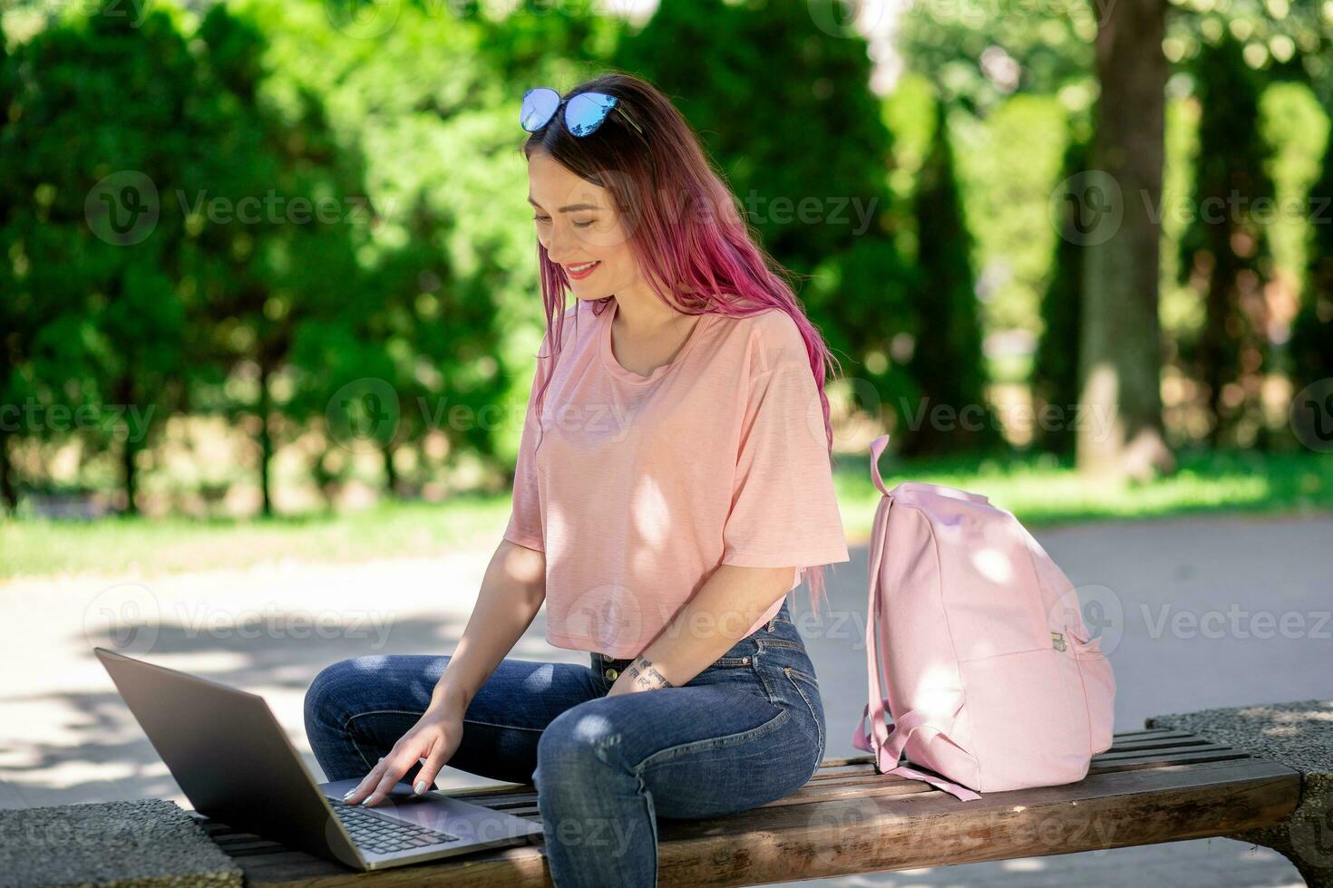 Jeune fille est en train d'étudier dans le printemps parc, séance sur le en bois banc et navigation sur sa portable photo