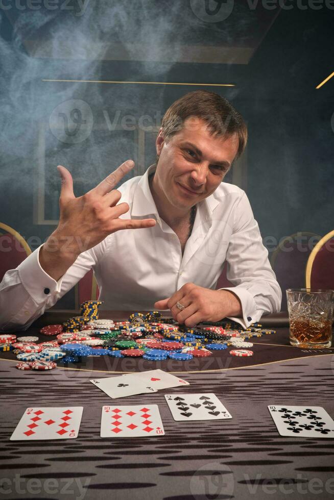 Beau émotif homme est en jouant poker séance à le table dans casino. photo