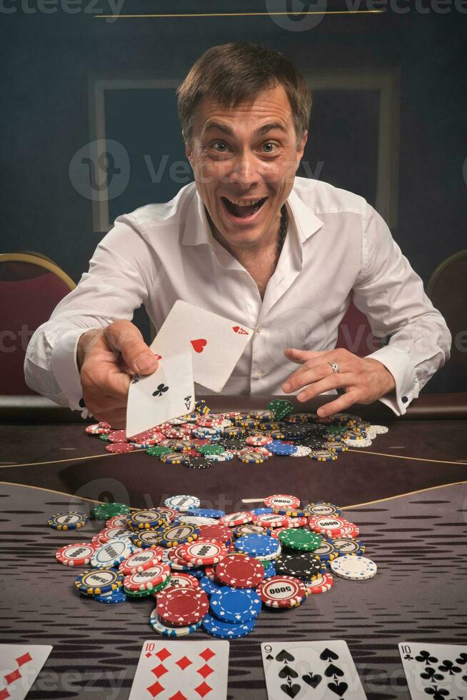 Beau émotif homme est en jouant poker séance à le table dans casino. photo