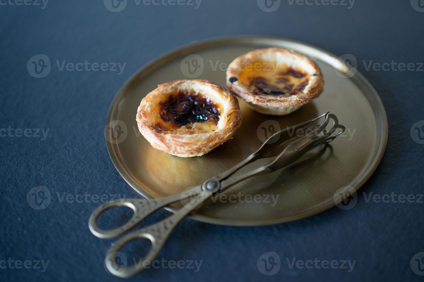 gros plan de deux délicieux gâteaux de belem, pasteis de belem sur un plateau en bronze, avec des pinces de service. suivant la recette traditionnelle portugaise. gastronomie portugaise. photo