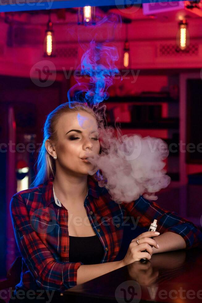 Jeune jolie femme dans une chemise dans une cage fumée un électronique cigarette à le vape bar photo