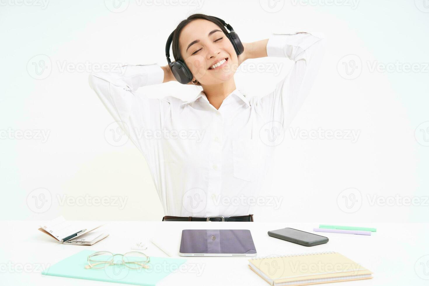 souriant femme d'affaires dans écouteurs, est assis à Bureau bureau écoute la musique et se détend, repose après travail, blanc Contexte photo