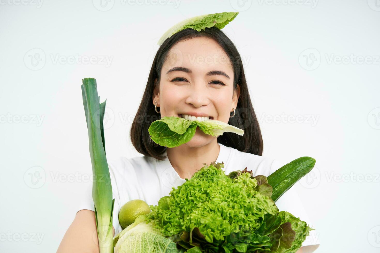 portrait de souriant coréen femme mange salade feuille, en portant vert légumes, en mangeant nutritif nourriture, blanc Contexte photo