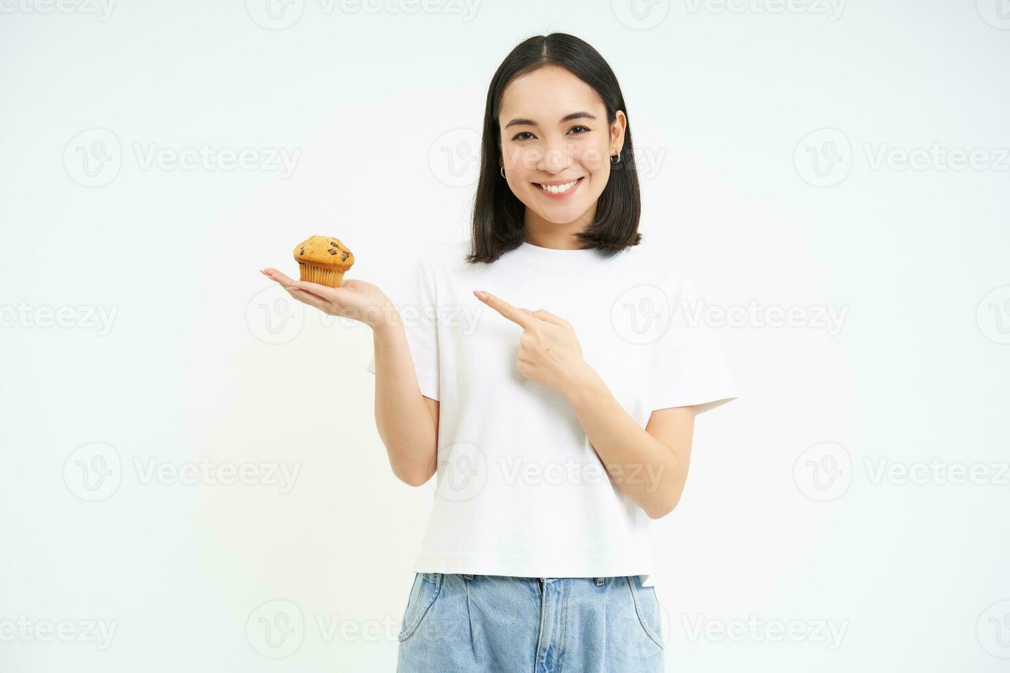 portrait de souriant Jeune femme montrer du doigt doigt à petit gâteau, montrant sa préféré boulangerie dessert, blanc Contexte photo