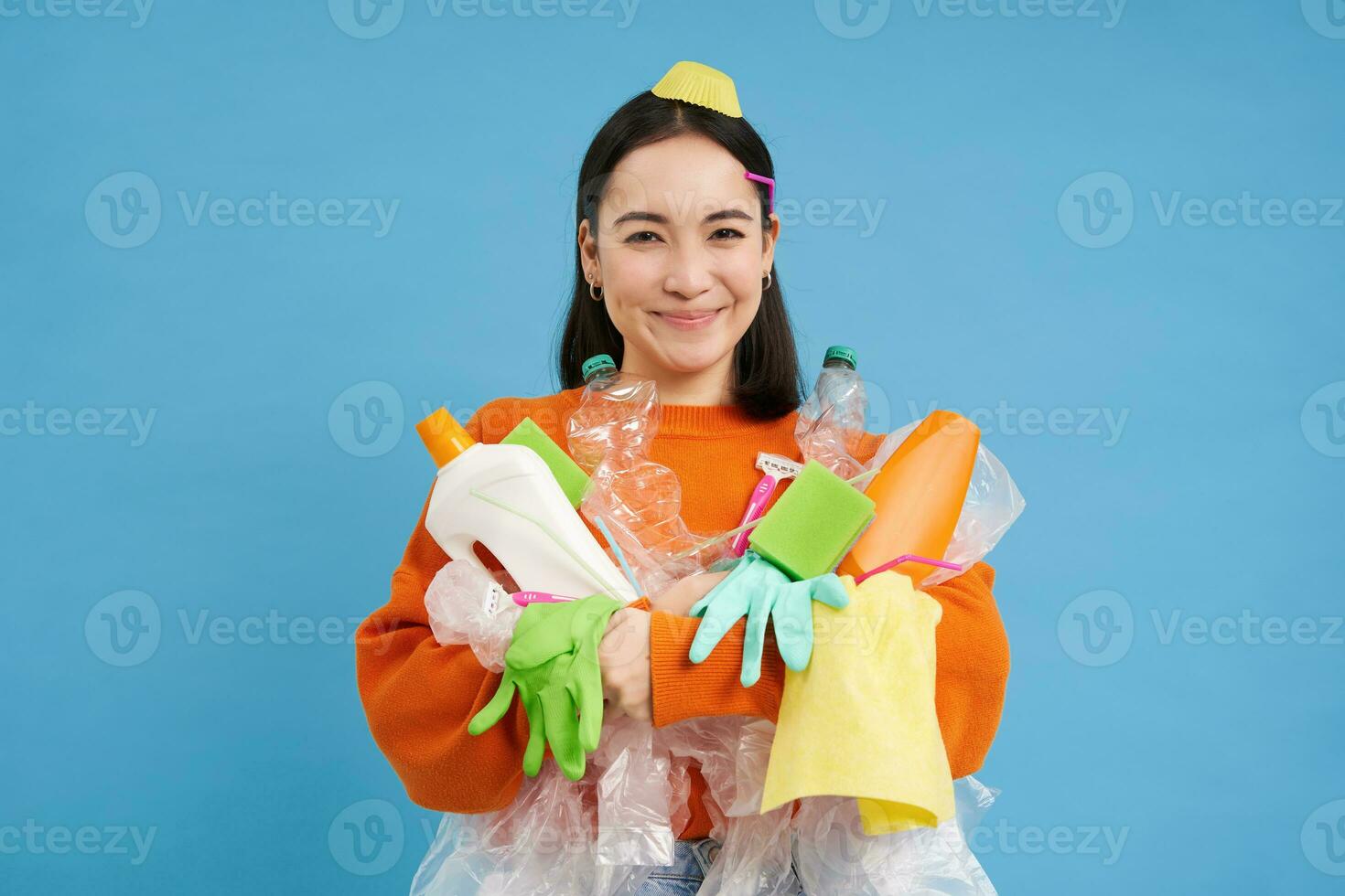 portrait de souriant coréen fille, en portant trié des ordures pour recyclage, regards content, se soucie pour la nature et environnement, bleu Contexte photo