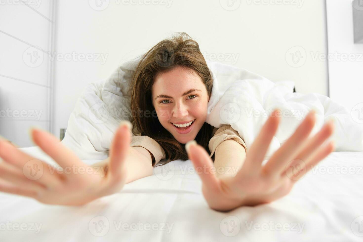 magnifique femme élongation, montrant sa bras dans caméra, mensonge dans lit, veille en haut dans Matin de bien sommeil ou sieste photo