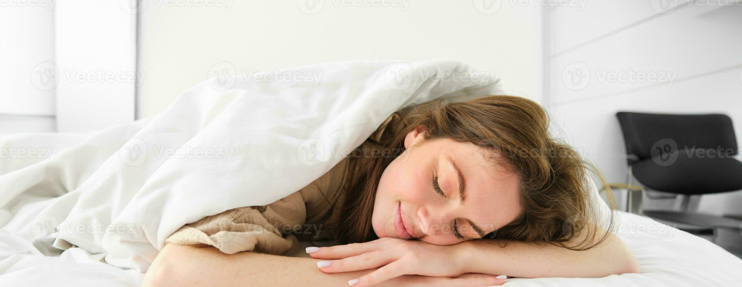 mignonne Jeune femme mensonge en dessous de couverture et souriant, dormant, ayant une bien Matin sieste, paresseux journée dans lit photo