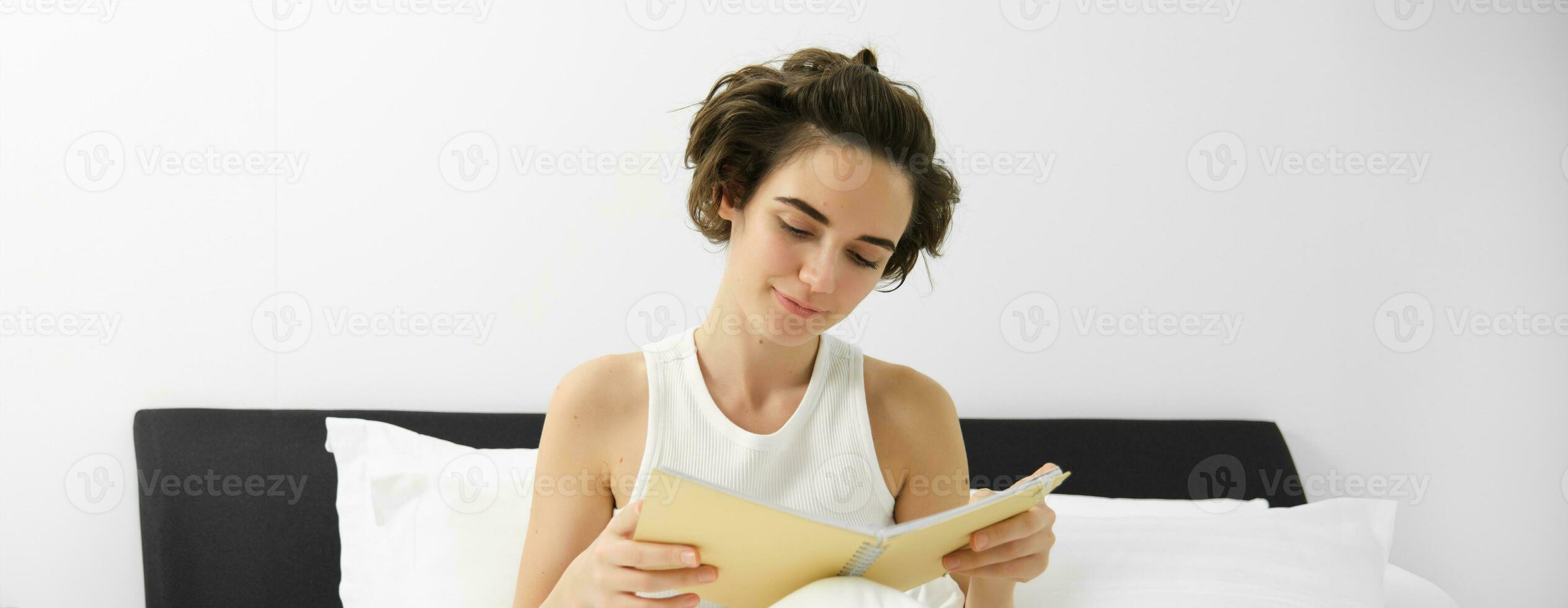 proche en haut portrait de Jeune femme, en train de lire journal, séance dans lit et en étudiant, réviser pour examen avant Aller à sommeil photo