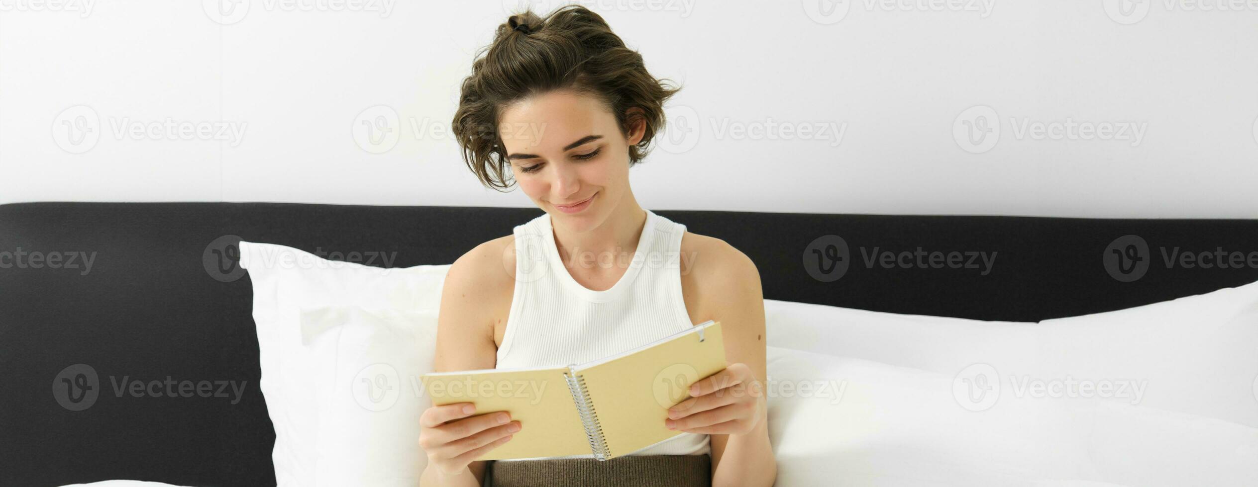 portrait de femme en train de lire sa planificateur et départ le jour, à la recherche à Remarques, séance sur lit dans Matin photo