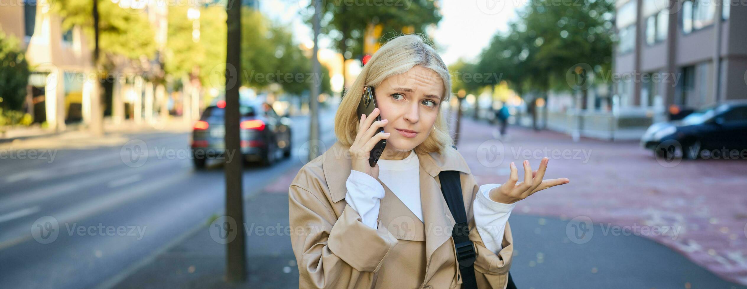 portrait de femme avec confus affronter, parlant sur mobile téléphone, répondre téléphone appel, permanent sur rue avec perplexe, Aucune idée expression, posant sur route photo