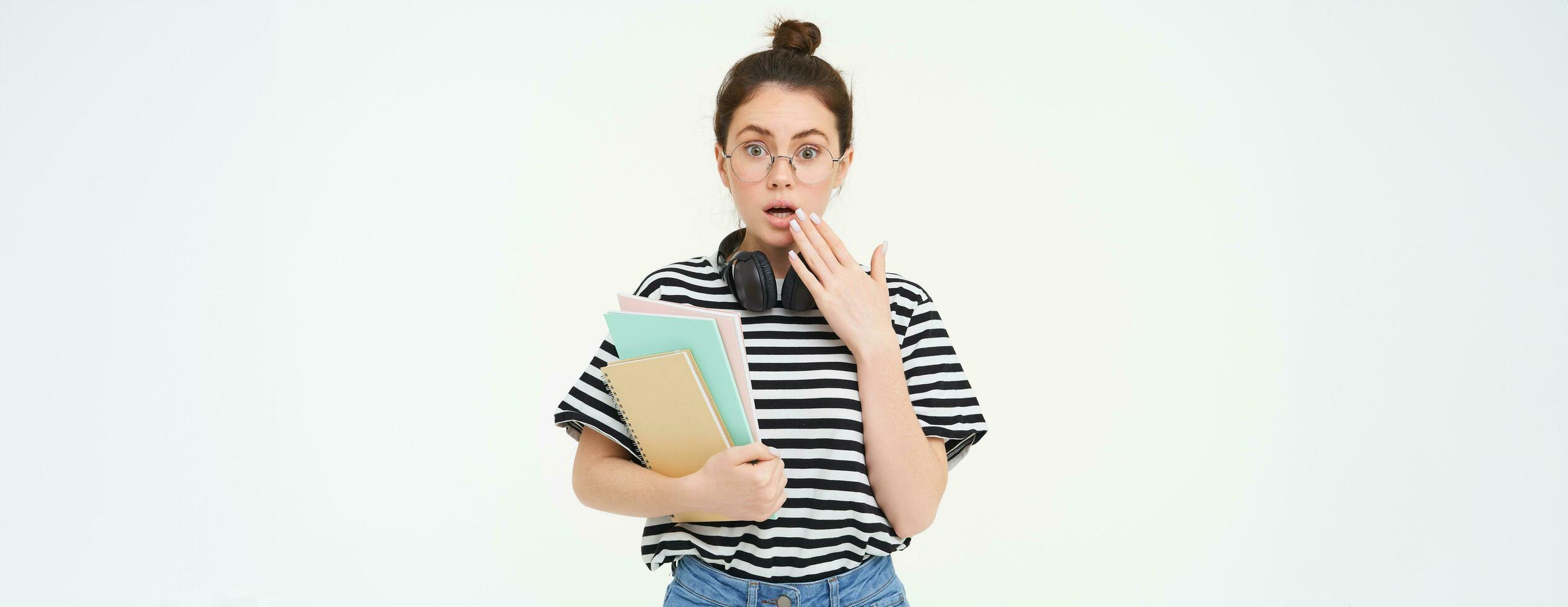 portrait de femme dans lunettes, étudiant regards surpris, halète et regards sous le choc à caméra, détient des cahiers et étude matériel, blanc Contexte photo