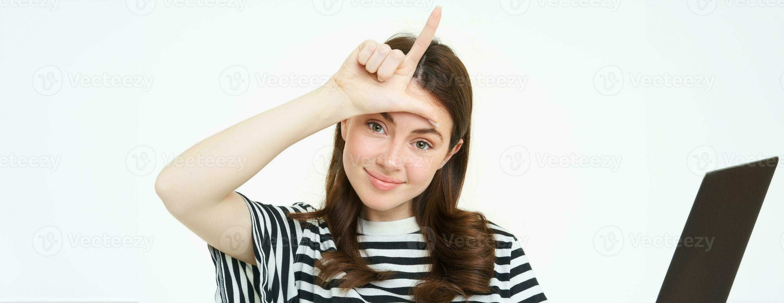 proche en haut portrait de Jeune brunette fille railleur toi, montrant perdant doigt geste, l lettre avec main sur front, souriant avec heureux affronter, permanent isolé sur blanc Contexte photo