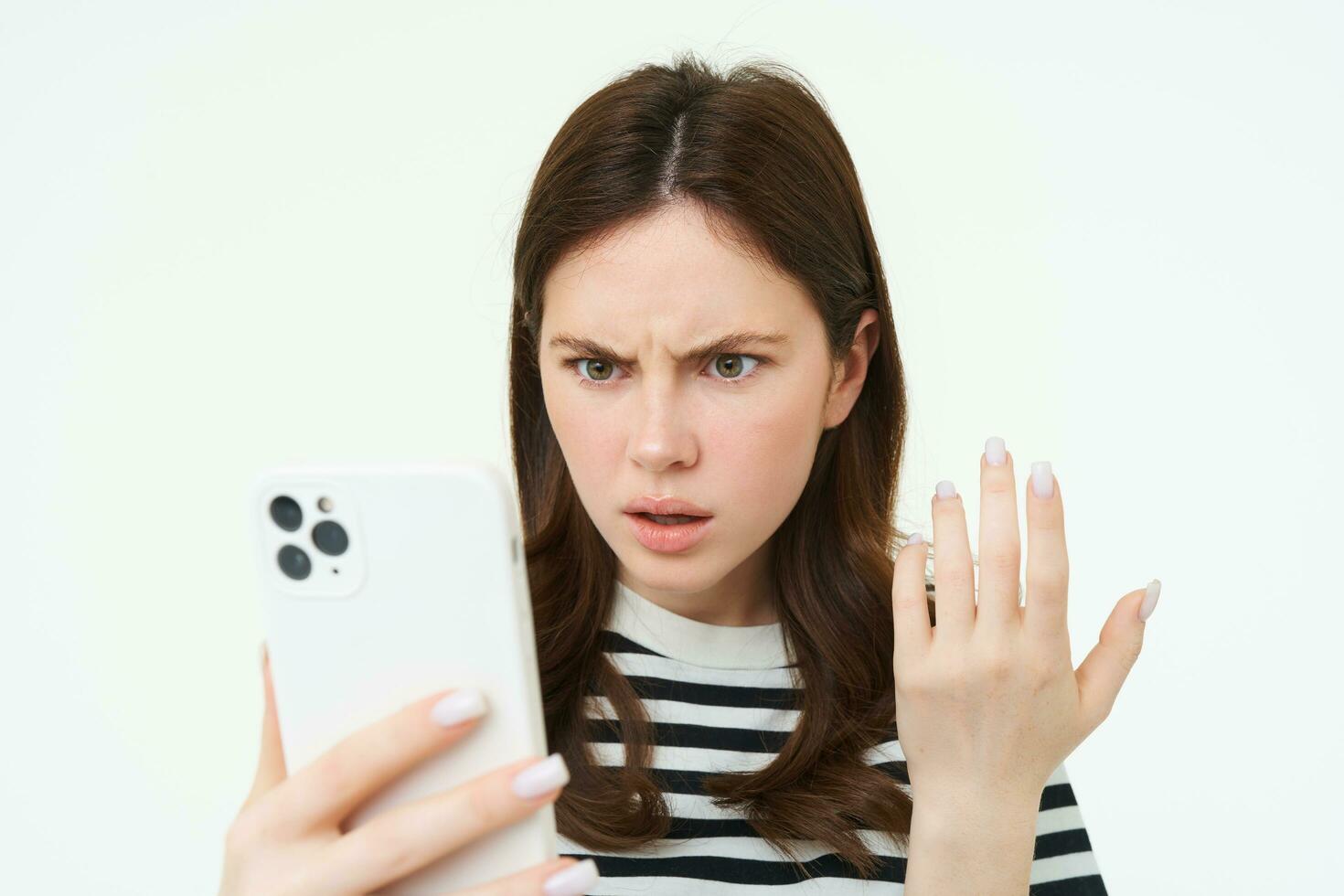 portrait de agacé fille regarder à sa mobile téléphone écran avec frustré affronter, blanc Contexte photo