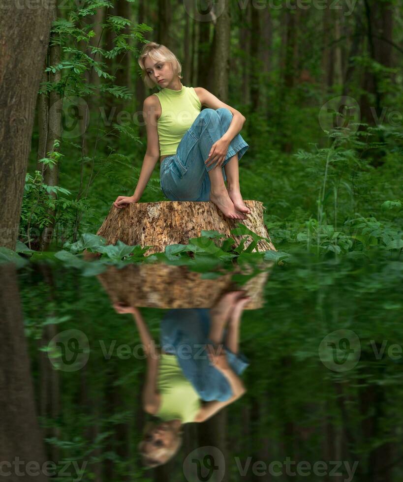 adolescent fille est assis sur une souche dans une Naturel forêt parc avec une triste et réfléchi regarder, réfléchi dans le l'eau photo