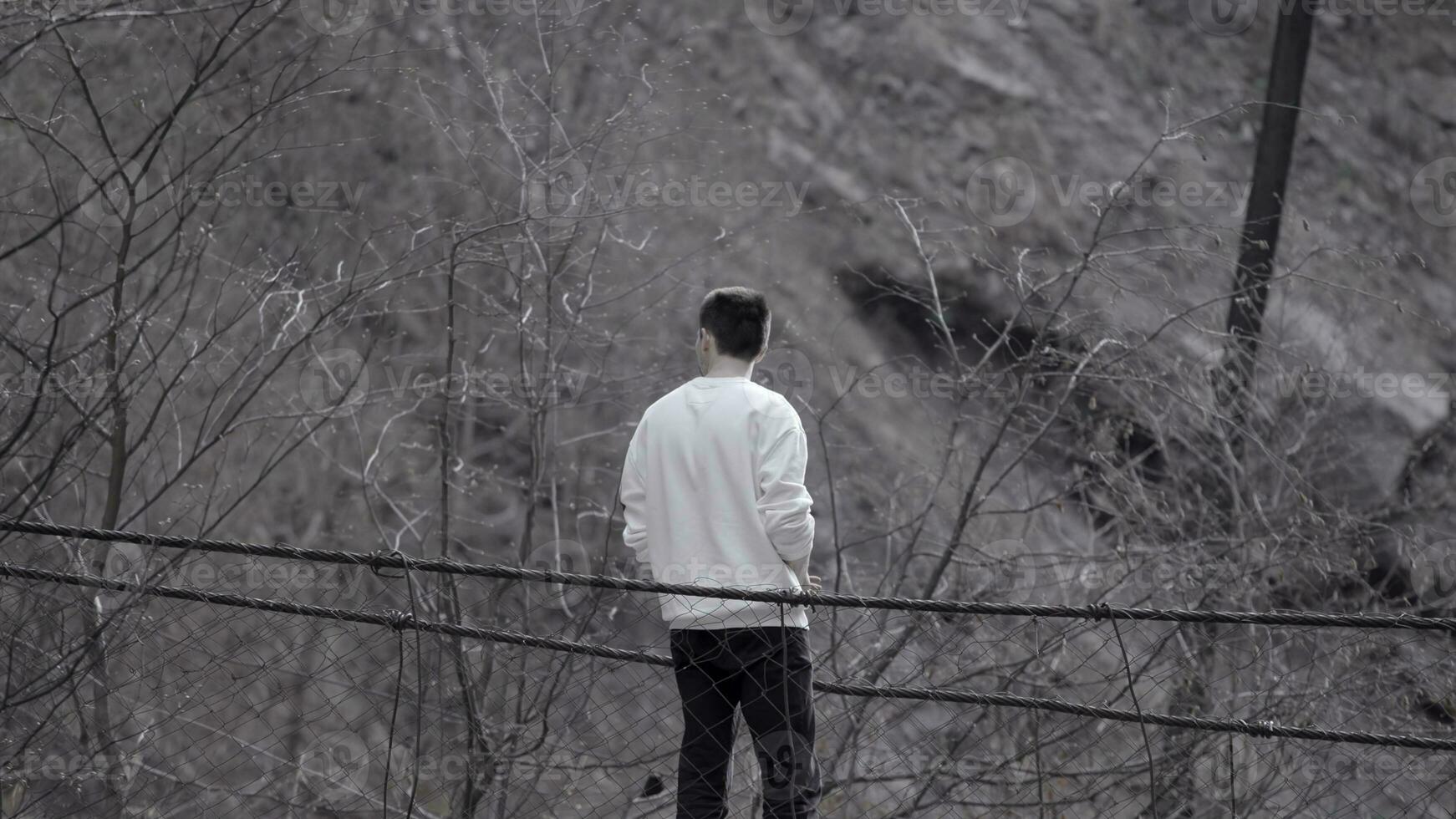 arrière vue de une homme permanent à le bord de un l'automne gris sale pente. Stock images. Jeune homme à la recherche réfléchi. photo