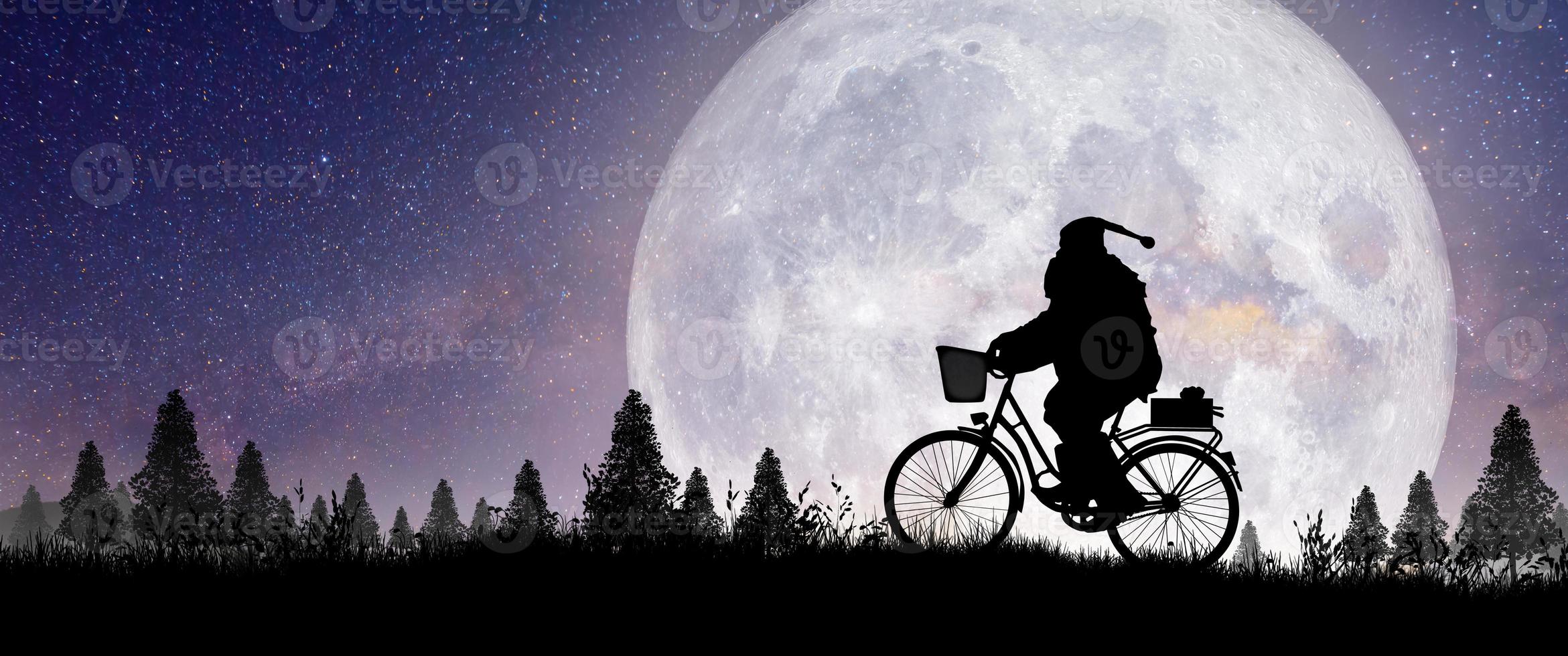silhouette du père noël à cheval sur son vélo pendant la pleine lune. photo