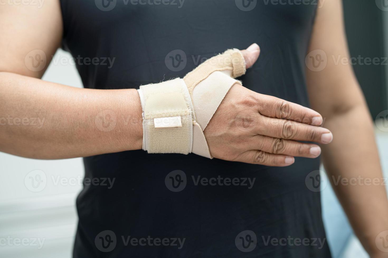 une femme asiatique d'âge moyen utilise un bandage élastique pour traiter le syndrome de de quervain à la main et au doigt au bureau. photo