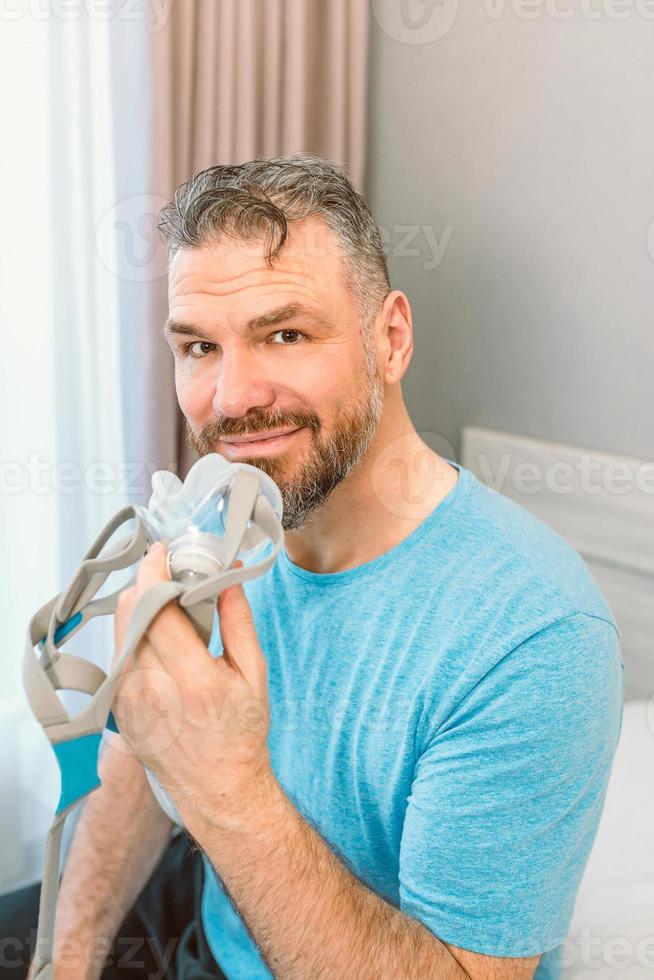 homme reposé heureux avec des problèmes respiratoires chroniques après avoir utilisé une machine cpap assis sur le lit dans la chambre. soins de santé, cpap, thérapie de l'apnée obstructive du sommeil, concept de ronflement photo