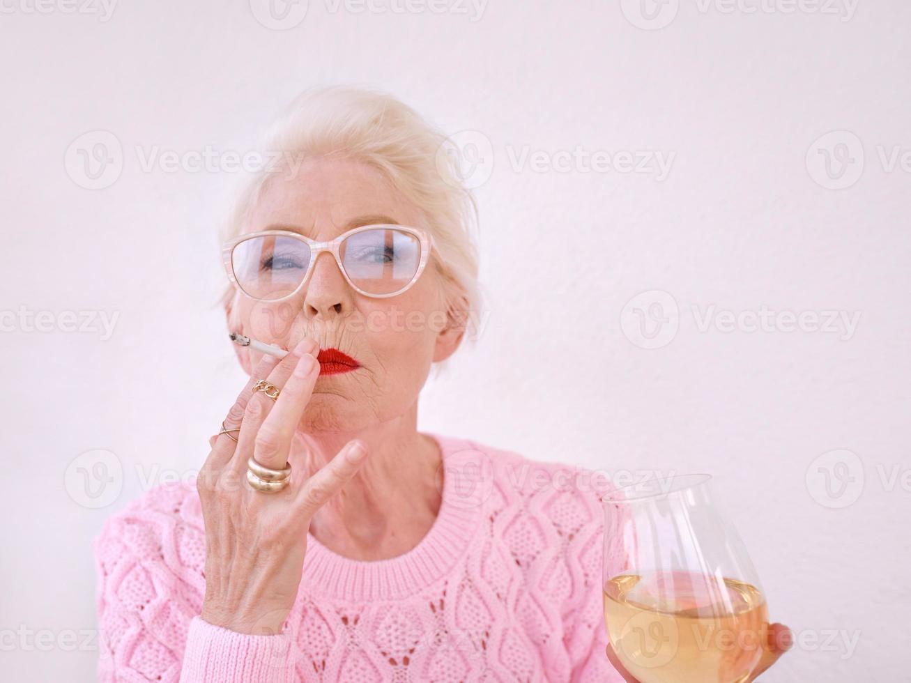 Old fashioned senior woman smoking cigarette avec verre de vin blanc. mauvaise habitude, concept de dépendance photo