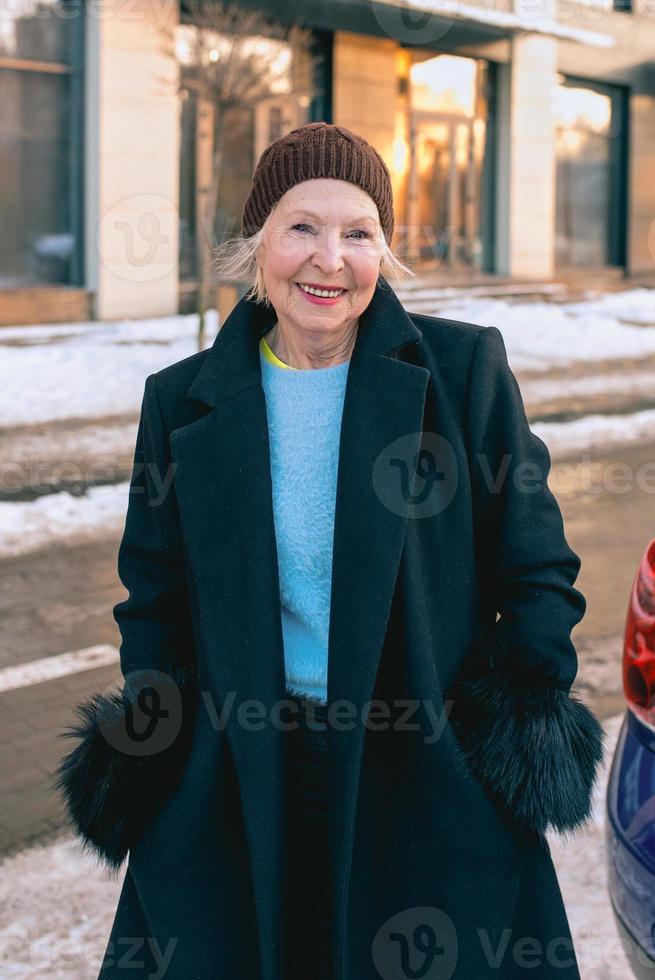 femme élégante senior en élégant manteau noir et sac à main marchant de sa voiture à un rendez-vous d'affaires. affaires, style, concept anti-âge photo