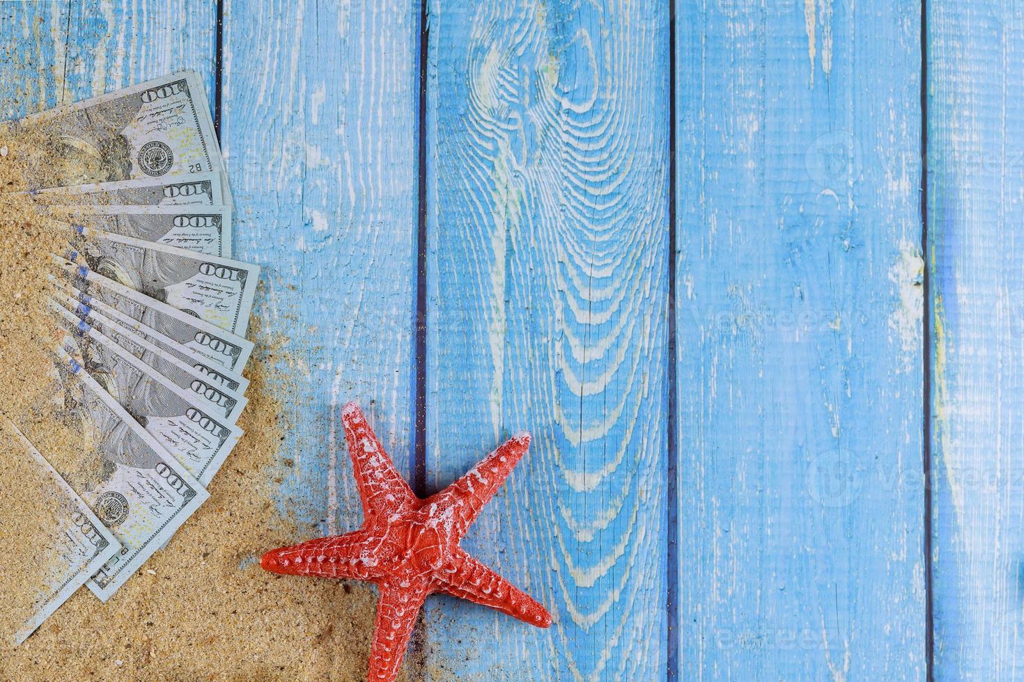 étoile de mer rouge sur la plage de sable et billet d'un dollar américain sur fond de bois bleu photo