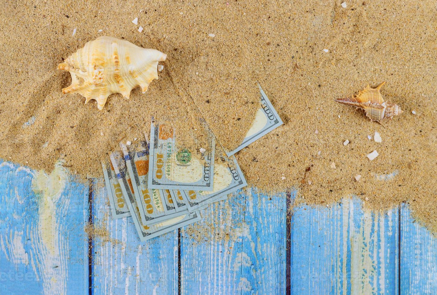 temps de voyager concept coquillages dans le sable de la plage sur des billets de cent dollars photo