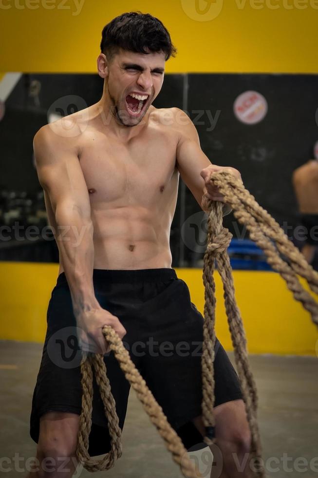 homme agressif puissant musclé s'entrainant avec une corde dans une salle de fitness d'entraînement fonctionnel photo