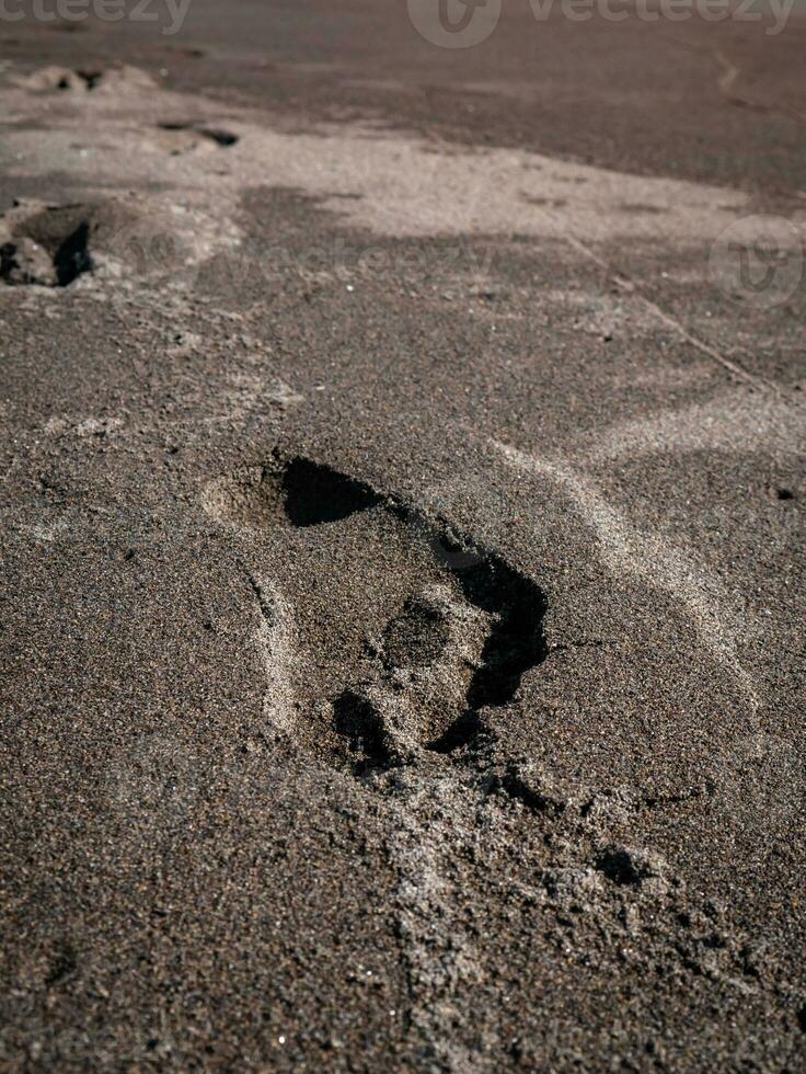 empreintes sur le noir le sable de le plage photo