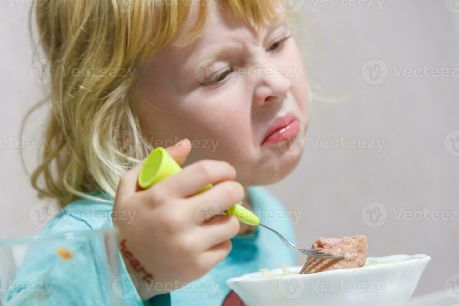 une peu fille a petit déjeuner à Accueil spaghetti avec saucisses. peu blond fille en mangeant dîner avec fourchette à table photo