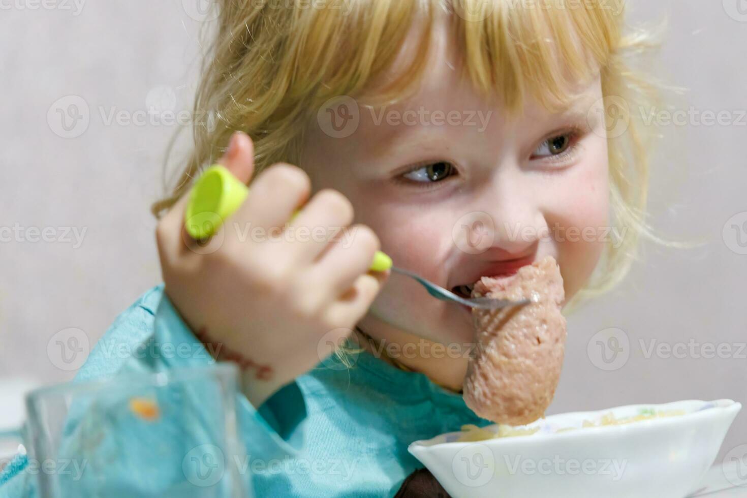 une peu fille a petit déjeuner à Accueil spaghetti avec saucisses. peu blond fille en mangeant dîner avec fourchette à table photo