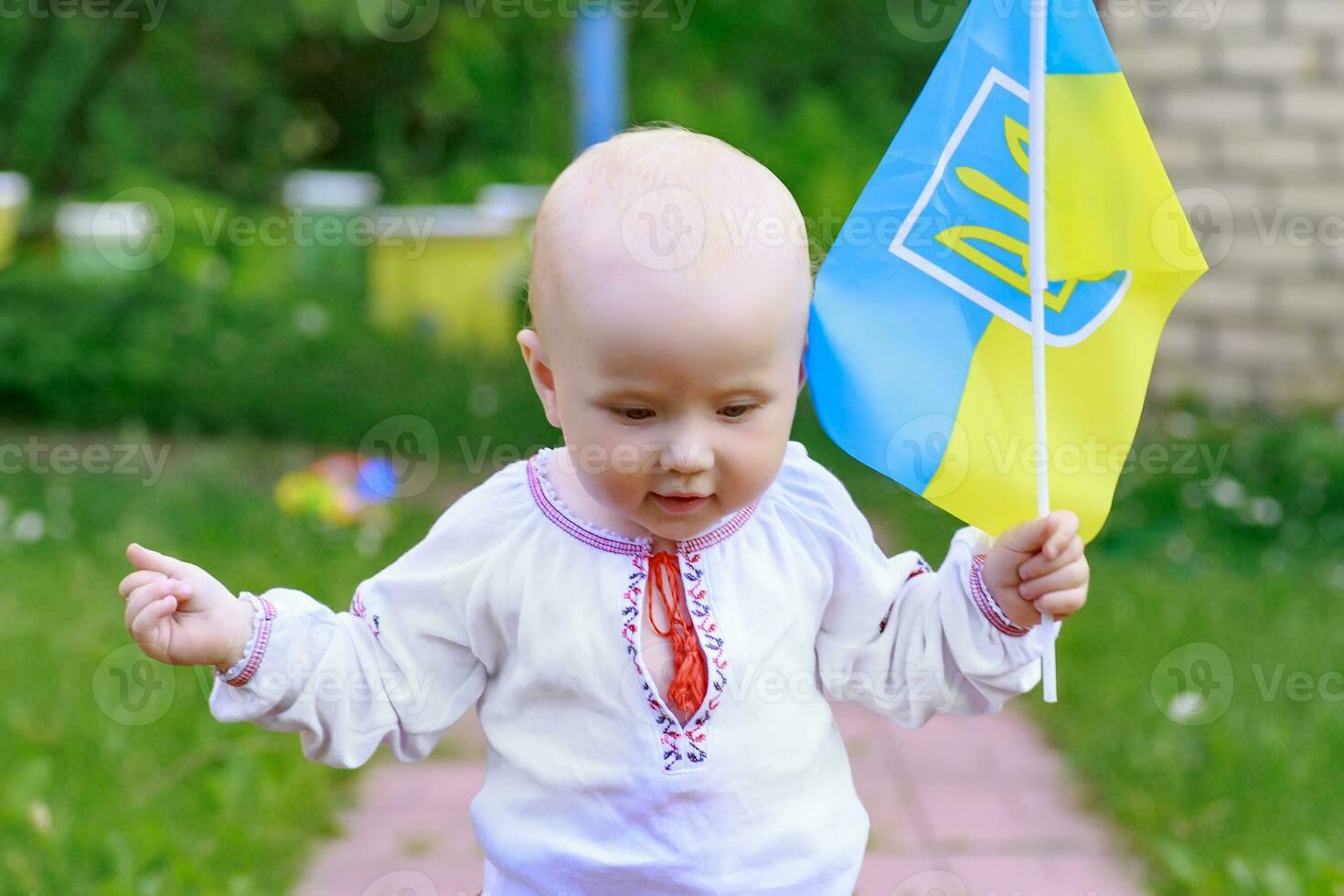 ukrainien drapeau dans le mains de une content peu enfant enfant en bas âge dans nationale costume. souriant bambin fille avec le drapeau de Ukraine. ukrainien bébé fait du le premier pas. photo