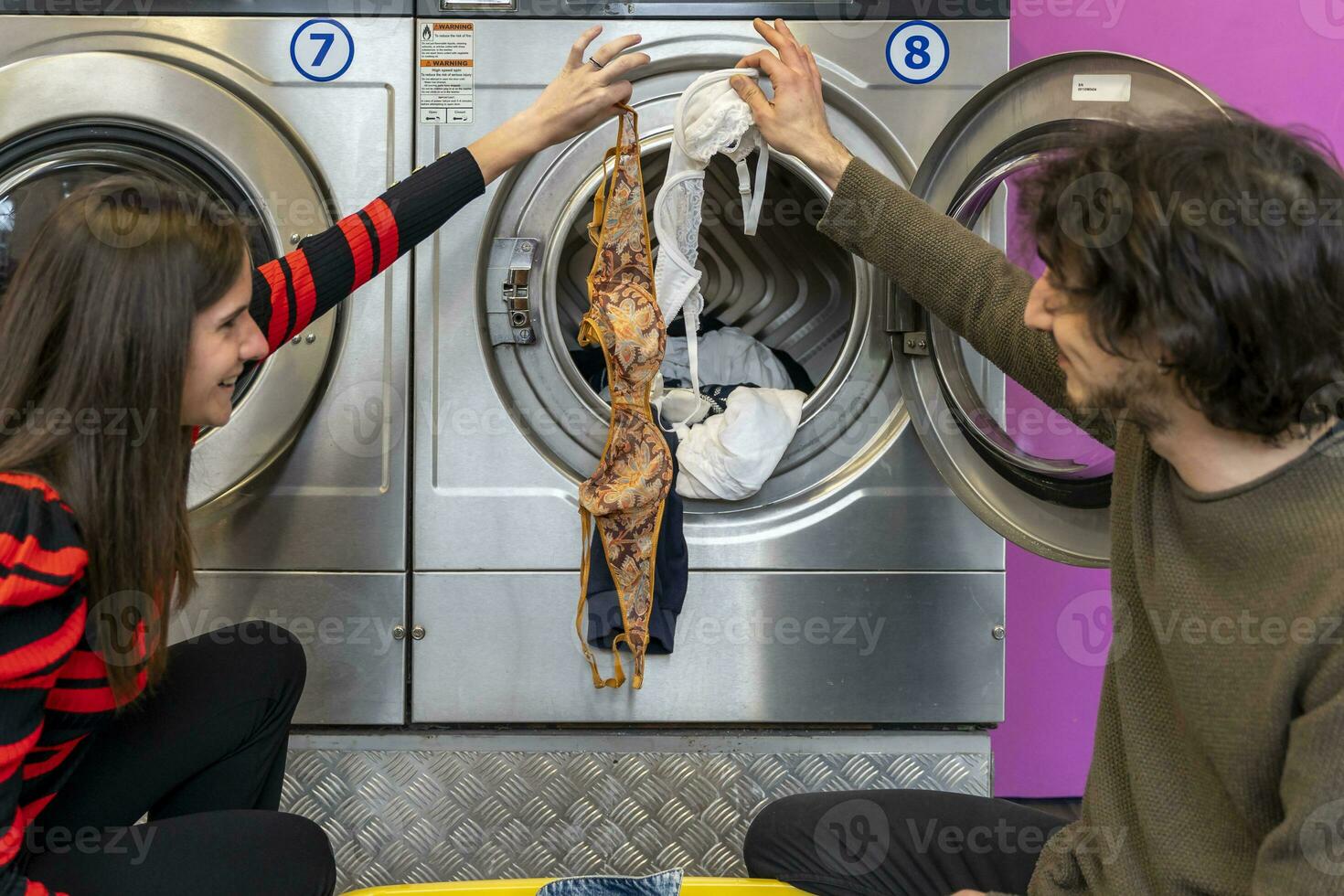 Jeune couple est en mettant vêtements dans le la lessive machine tambour photo