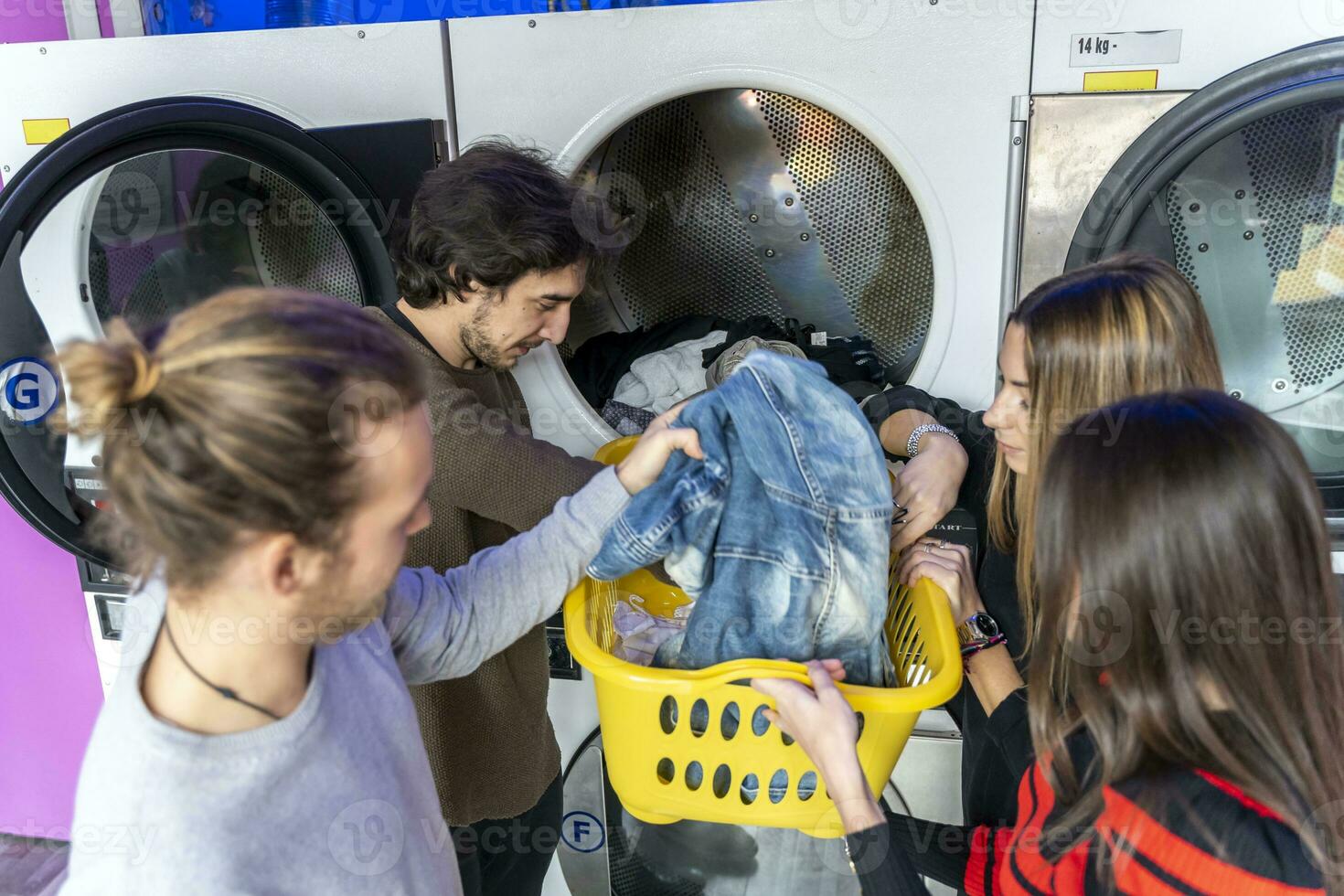 Jeune groupe de millénaire copains est en mettant vêtements dans le la lessive machine photo