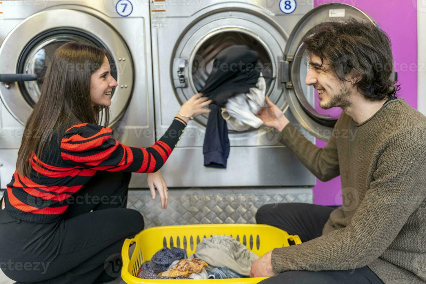 Jeune couple est en mettant vêtements dans le la lessive machine tambour photo