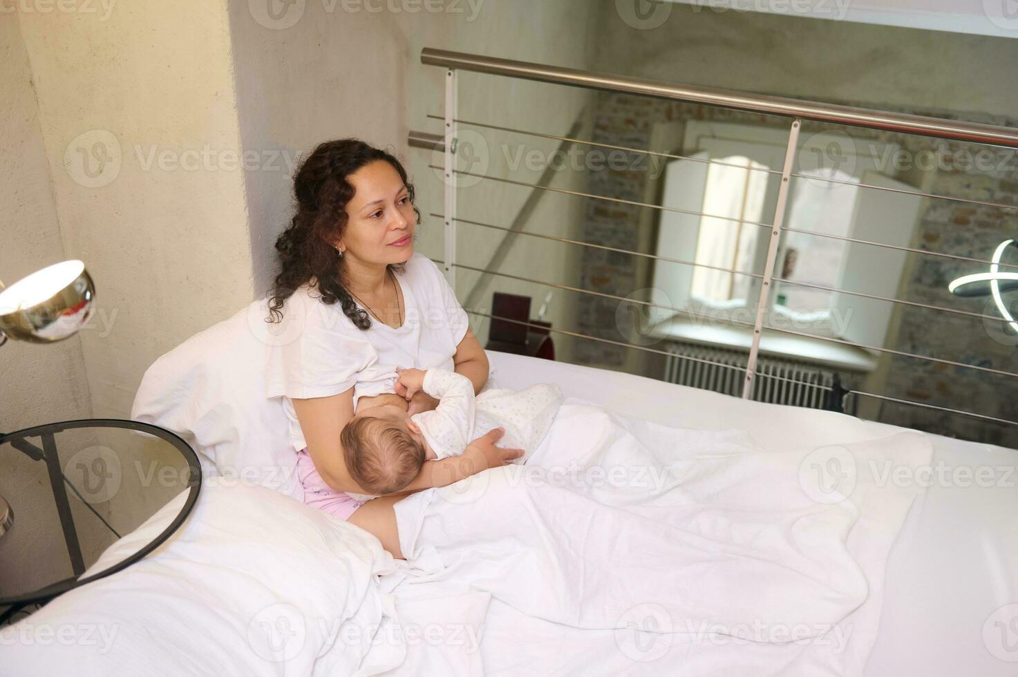 aérien vue de une aimant soins mère et sa mignonne nouveau née bébé sourit à la recherche à sa bébé garçon tandis que allaitement maternel lui photo