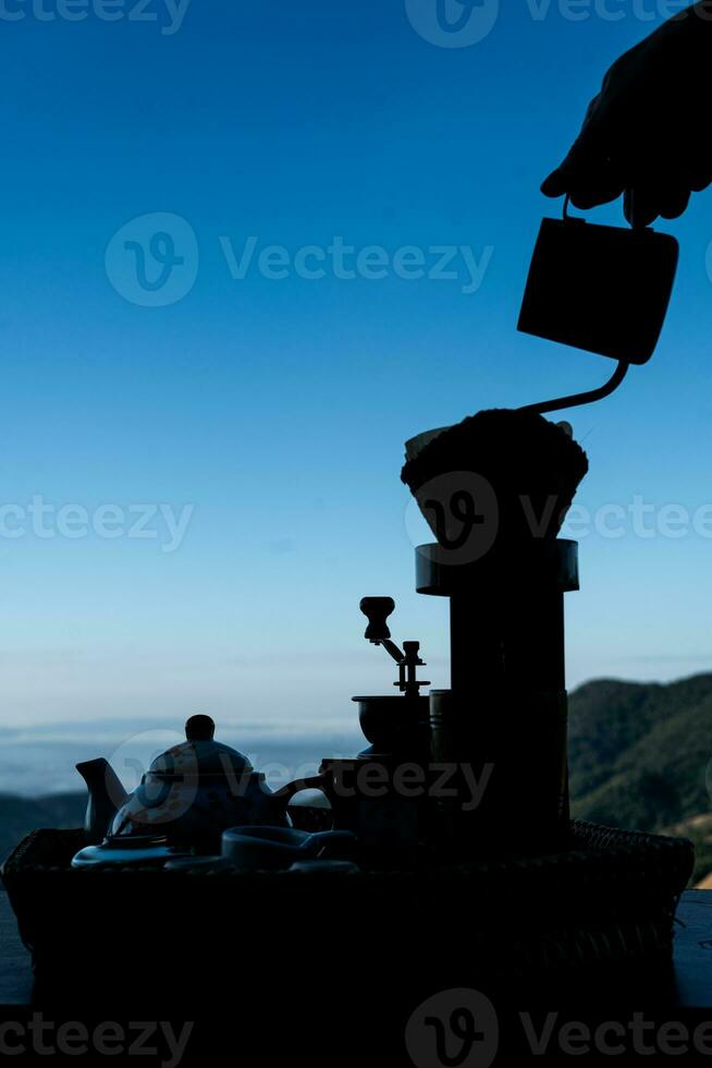 silhouette de le femme fabrication goutte café sur le en bois table et une magnifique ciel et montagnes Contexte photo