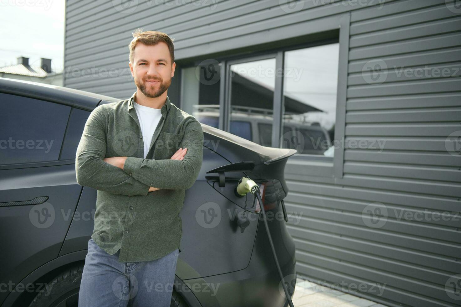 Beau barbu homme dans décontractée porter, permanent à le mise en charge station et chargeur pour un électrique auto. éco électrique voiture concept photo