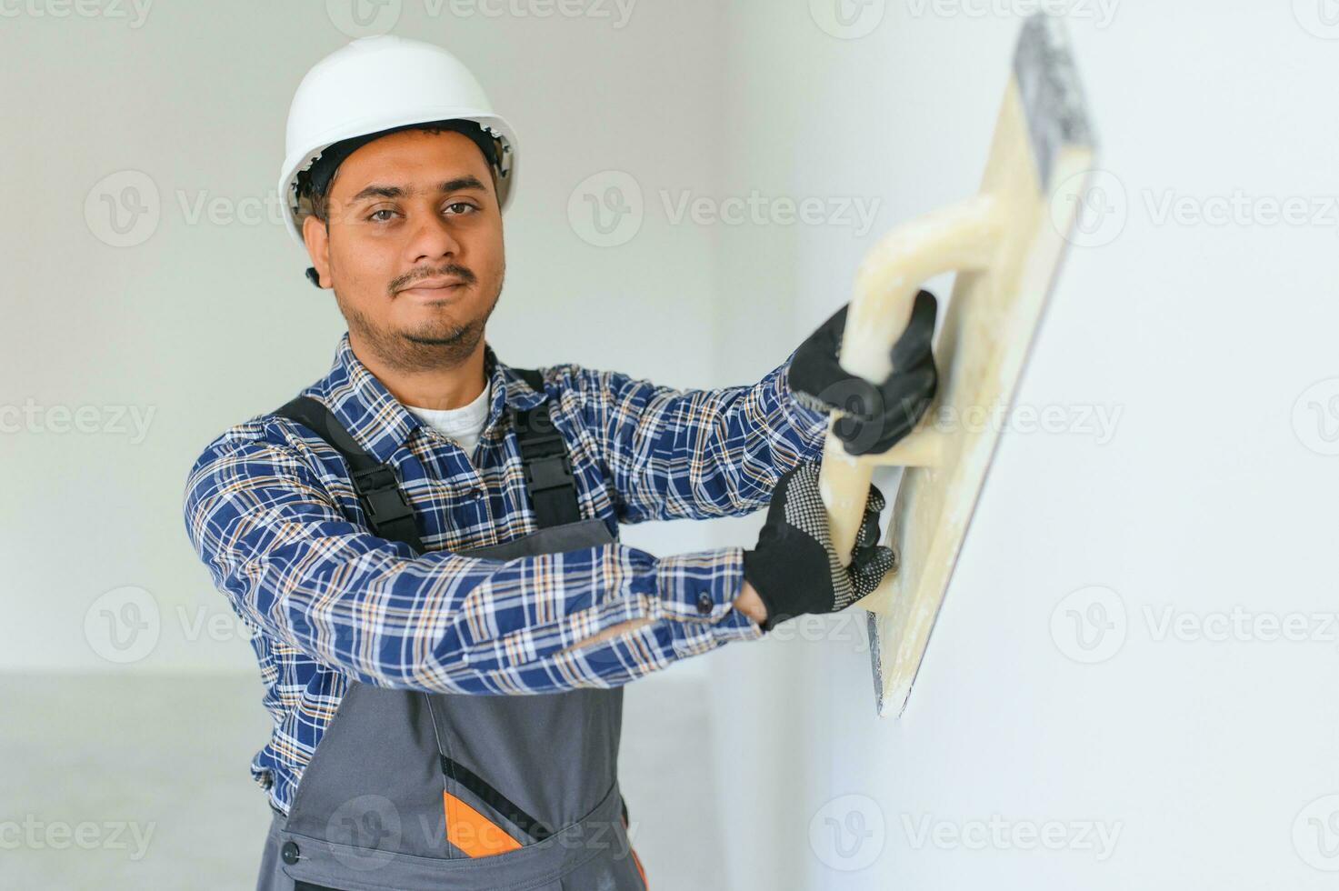 un Indien ouvrier travaux dans un vide appartement. une homme dans une uniforme fait du réparations à l'intérieur le bâtiment photo
