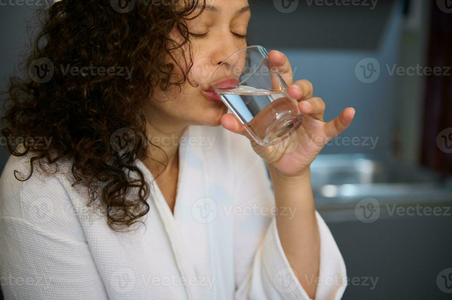 fermer frisé aux cheveux jolie femme fabrication siroter de l'eau tandis que prise médecine, une anti douleur ou nutritionnel supplément photo