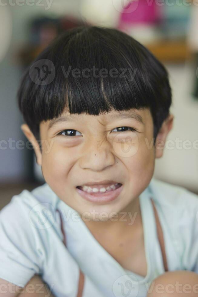 proche en haut portrait de asiatique garçon avec noir frange, noir yeux avec une souriant visage portant une lumière vert chemise Regardez à caméra et séance sur le sol de le sien maison et main en portant crayon à dessiner. photo