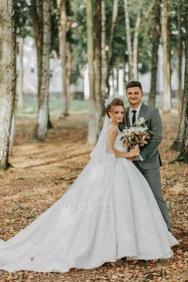 la mariée et jeune marié sur le Contexte de une Conte de fée forêt. Royal mariage concept. le jeune marié embrasse le la mariée. tendresse et calme. toute la longueur portrait photo