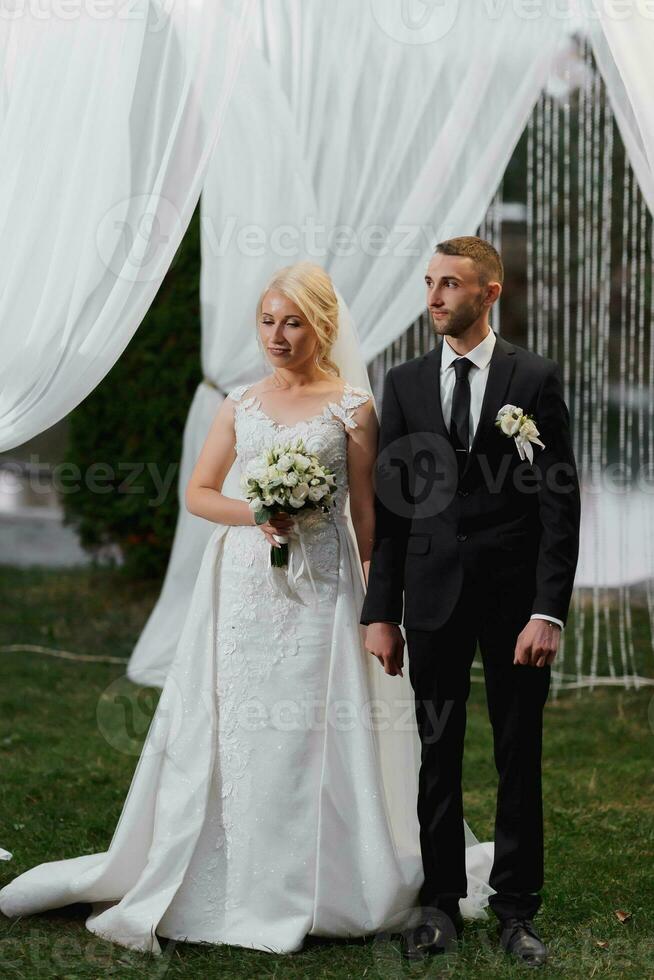 mariage portrait. le la mariée et jeune marié supporter par le cambre pendant le La peinture cérémonie. soir La peinture cérémonie. photo