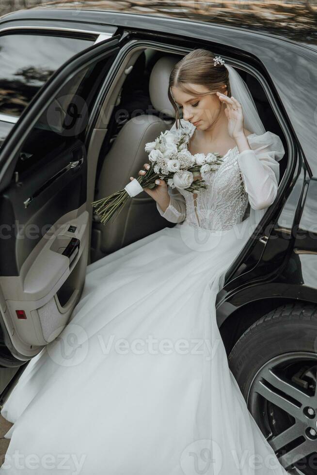 magnifique la mariée avec branché maquillage et coiffure dans luxe mariage robe dans noir mariage voiture séance sur retour siège et posant pour photographe photo