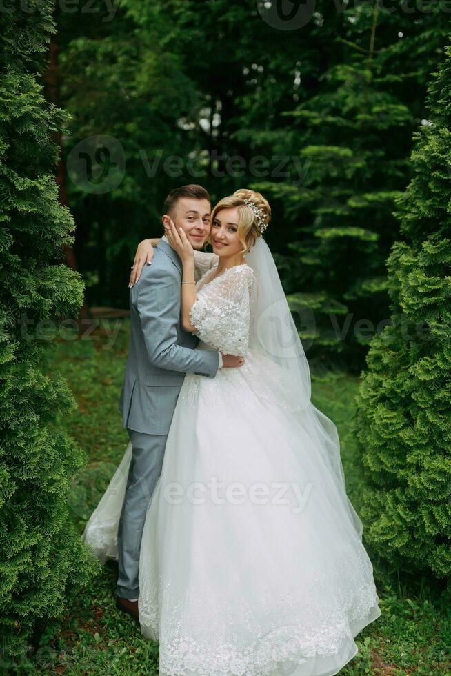 portrait de le la mariée et jeune marié permanent sur le Contexte de vert des arbres, embrassant. le la mariée sourit sincèrement. élégant jeune marié. mode et style. magnifique la mariée photo