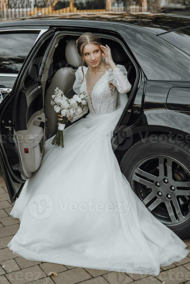 magnifique la mariée avec branché maquillage et coiffure dans luxe mariage robe dans noir mariage voiture séance sur retour siège et posant pour photographe photo