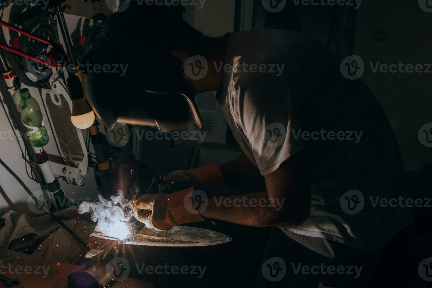 une soudeur est Faire soudage travail dans le sien garage tandis que des étincelles mouche autour, il est portant une sécurité casque. Manuel travail avec une soudage dispositif photo