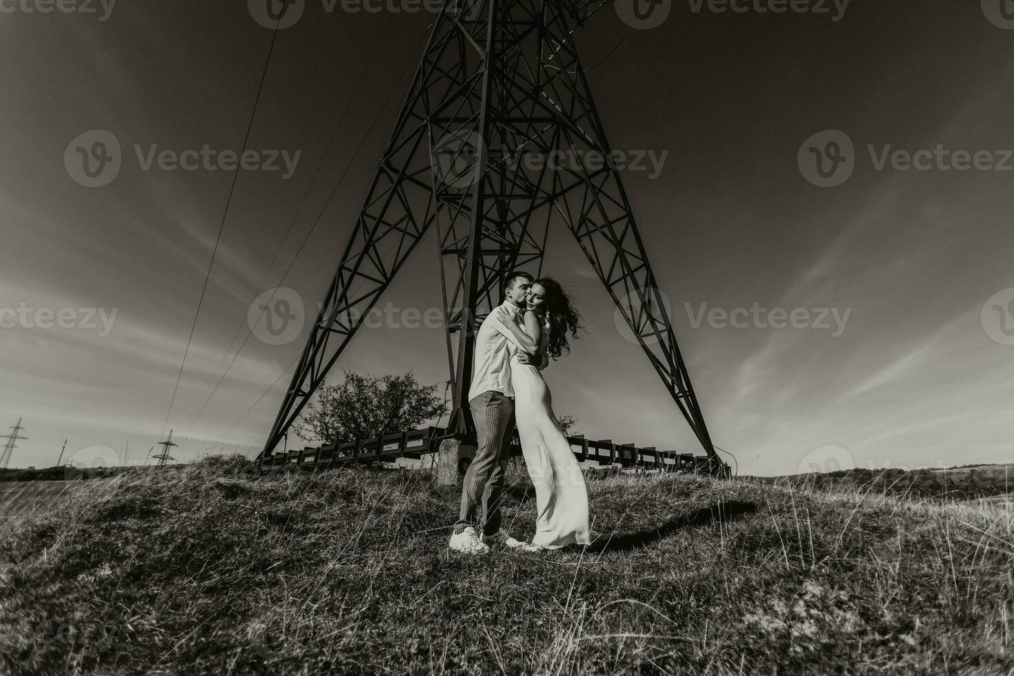 élégant modèle couple dans le montagnes dans été. une Jeune garçon et fille dans une blanc soie robe sont permanent près grand les structures de Puissance lignes. noir et blanc contraste photo