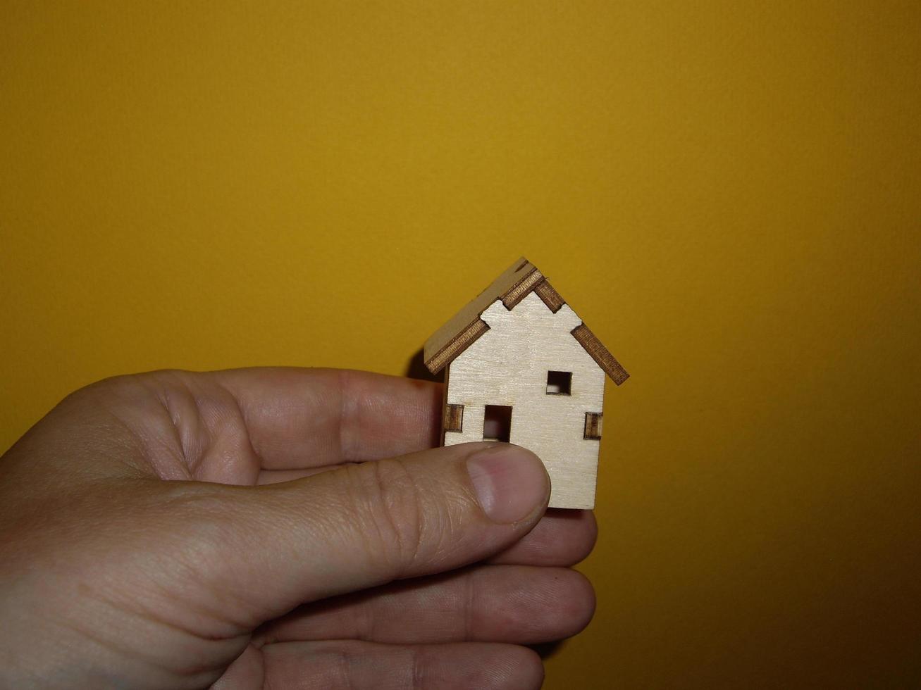 petite maison en bois dans la main d'un homme sur fond jaune photo