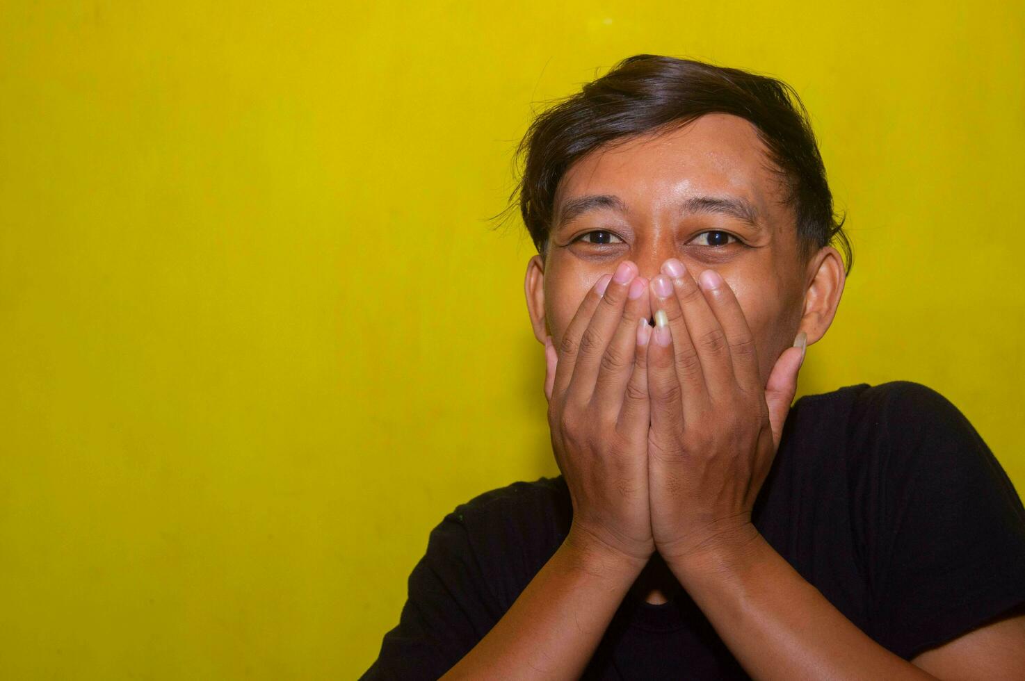 gresik, Indonésie, 5 décembre 2023 - le expression de une Jeune homme qui est couvrant le sien bouche car il est en portant retour rire. photo