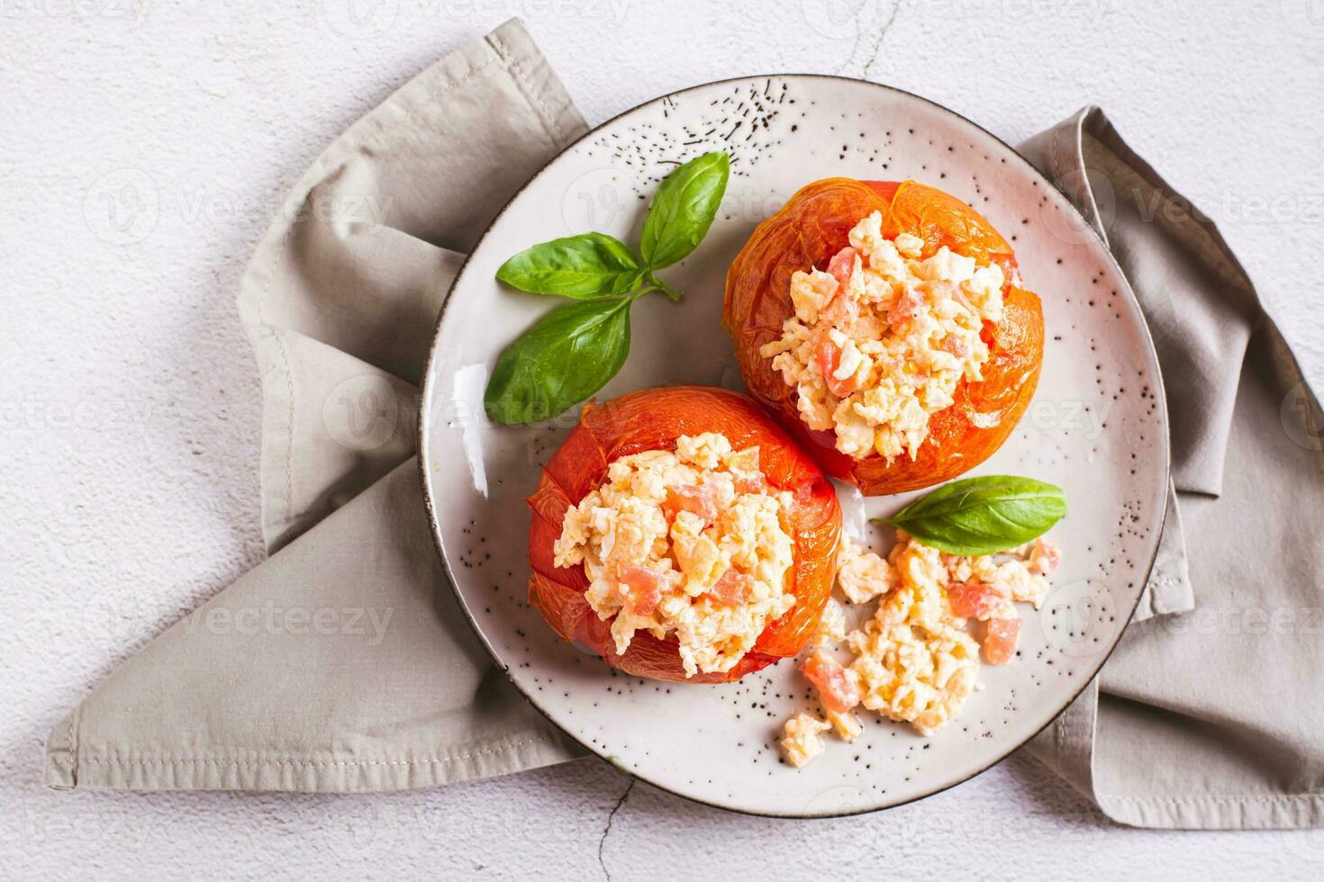 proche en haut de cuit tomate moitiés rempli avec brouillé Oeuf et basilic sur une assiette Haut vue photo